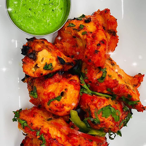 A plate of red-orange chicken tikka with a bowl of green chutney.